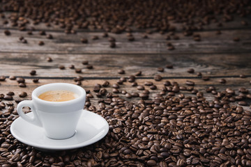 White cup of coffee espresso with beans on brown wooden table