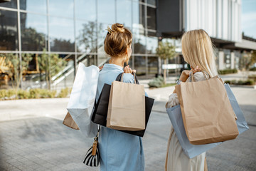 Two women holding empty shopping bags with copy space, while standing back near the shopping mall