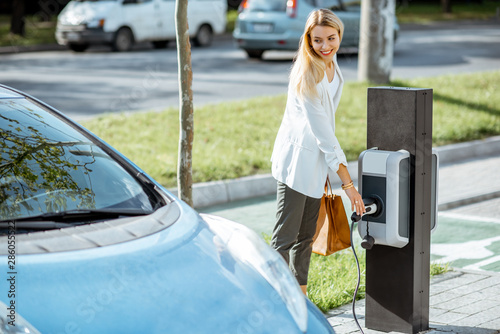 Fotografía Businesswoman plugging charging gun into the electric gas station on the car par