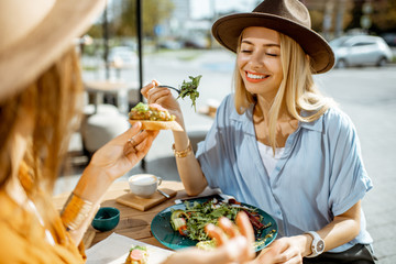 two female best friends eating healthy food while sitting together on a restaurant terrace on a summ