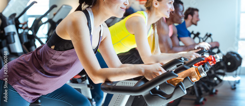 Fotomural Asian woman and her friends on fitness bike in gym