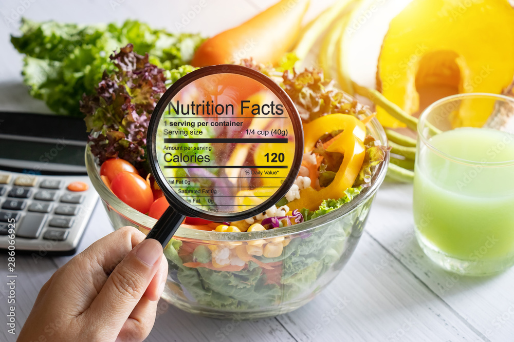 nutritional information concept. hand use the magnifying glass to zoom in to see the details of the nutrition facts from food , salad bowl - obrazy, fototapety, plakaty 
