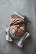 Flat-lay of freshly baked sourdough bread loaf and bread slices on rustic wooden board over grey concrete table background, top view, vertical composition
