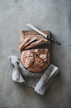 Flat-lay Of Freshly Baked Sourdough Bread Loaf And Bread Slices On Rustic Wooden Board Over Grey Concrete Table Background, Top View, Vertical Composition