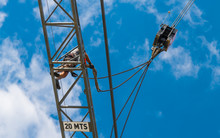 Tower Crane Installation. Hoist Device Detail. Work At Heights. Working Man On Steel Boom Of Lifting Machine. Blue Sky Background. Dangerous Building Work, Belaying. Occupational Safety. Bottom View.