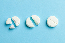 White Pills On Blue Background. Few Pills Broken In Half, Reducing The Dose Of The Medicine