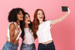 © Drobot Dean - Cute happy positive young three multiethnic girls friends posing isolated over pink wall background take a selfie by mobile phone.