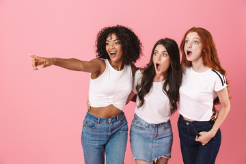 Wall Mural - three shocked emotional cute multi-ethnic girls friends posing isolated over pink wall background po