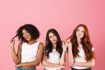 Thinking thoughtful young three multiethnic girls friends posing isolated over pink wall background.