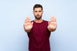© luismolinero - Handsome man over isolated blue background making stop gesture and disappointed