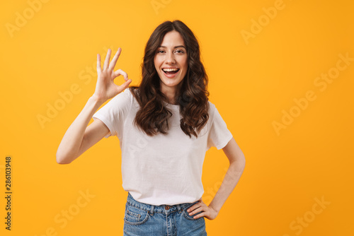 Fotomural Image of amazed brunette woman wearing casual clothes smiling and showing ok sig