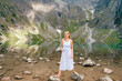 Funny girl with facial expression posing in white dress in lake with reflections among High Tatry mountains