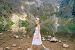 Funny girl with facial expression posing in white dress in lake with reflections among High Tatry mountains