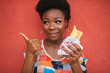 Cheerful african american girl with burger in her hand shows thumb up gesture over red wall on background.