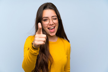 Wall Mural - teenager girl over isolated blue wall points finger at you