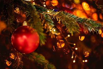 decorated christmas tree on blurred background with golden sparkling bokeh lights and red ball. fest