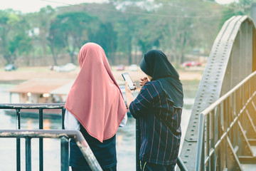 Wall Mural - Back view of Muslim women relax and admire the beautiful scenery in the evening on The Bridge of the River Kwai in Kanchanaburi, Thailand.