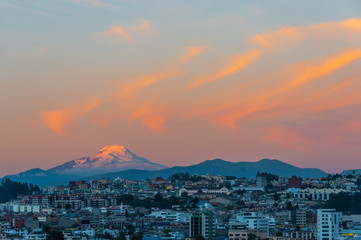 The majestic snowcapped Andes peak of the Cayambe volcano illuminated at sunset with the cityscape of Quito, Ecuador.