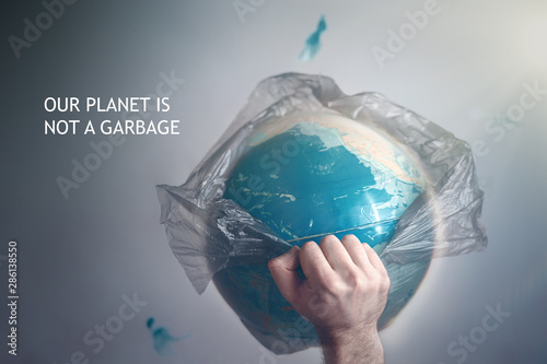Fotomural A man breaks a garbage bag which is wrapped globe of planet Earth