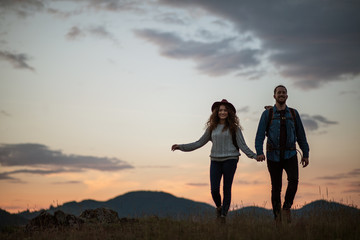 Wall Mural - young tourist couple travellers with backpacks hiking in nature at dusk.