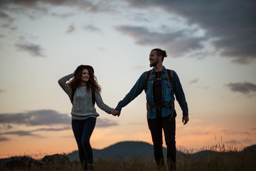 Wall Mural - young tourist couple travellers with backpacks hiking in nature at dusk.