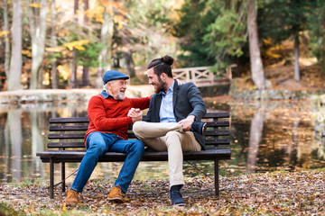 Wall Mural - Senior father and his son sitting on bench by lake in nature, talking.