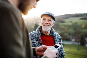 young man and his senior father on a walk in nature, using smartphone.