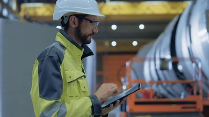 Wall Mural - Heavy Industry Engineer Walk Through Pipe Manufacturing Factory, Use Digital Tablet Computer. Facility for Construction of Oil, Gas and Fuel Pipeline Transportation Products. Side View Slow Motion