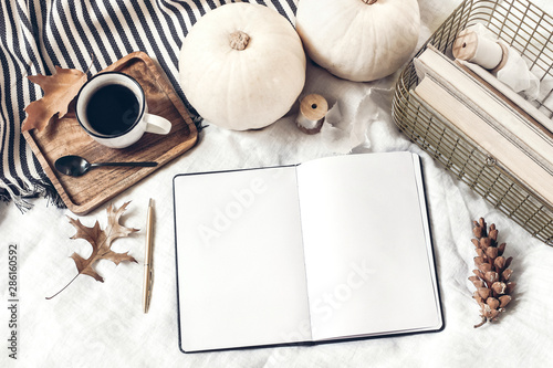 Autumn breakfast in bed composition. Blank open notepad, diary mockup. Cup of coffee, white pumpkins, plaid, oak leaves and old books. Linen background. Thanksgiving, Halloween. Flat lay. Top view.