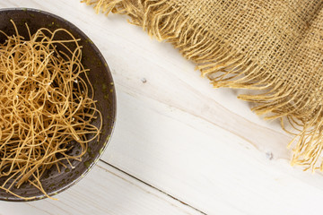 Lot of pieces of thin raw pasta noodles on grey plate with jute cloth flatlay on white wood