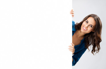 Happy smiling beautiful businesswoman showing blank sign board with empty copyspace area for some slogan or advertising text message, isolated against grey color background