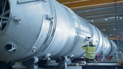 Wall Mural - Heavy Industry Engineer Uses Augmented Reality Digital Tablet to Scan Large Diameter Pipe. Modern Industrial Manufacturing Technology to Design and Construct Oil, Gas and Fuels Transport Pipeline.