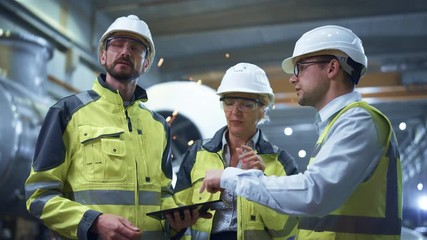 Wall Mural - Three Heavy Industry Engineers Stand in Pipe Manufacturing Factory, Use Digital Tablet Computer, Have Discussion. Large Pipe Assembled. Design and Construction of Oil, Gas and Fuels Transport Pipeline