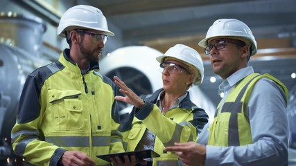 Wall Mural - 
Three Heavy Industry Engineers Stand in Pipe Manufacturing Factory, Use Digital Tablet Computer, Have Discussion. Large Pipe Assembly. Design and Construction of Oil, Gas and Fuels Transport Pipeline