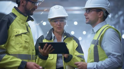 Wall Mural - Three Heavy Industry Engineers Stand in Pipe Manufacturing Factory, Use Digital Tablet Computer, Have Discussion. Large Pipe Assembled. Design and Construction of Oil, Gas and Fuels Transport Pipeline