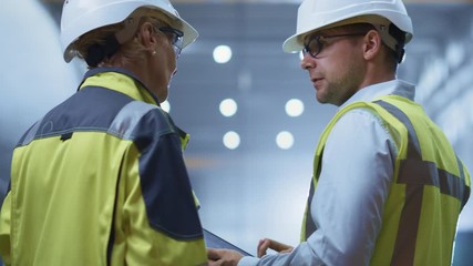 Wall Mural - Two Heavy Industry Engineers Stand in Pipe Manufacturing Factory, Use Digital Tablet Computer, Have Discussion. Construction of Oil, Gas and Fuels Transport Pipeline. Back View Sparks Flying