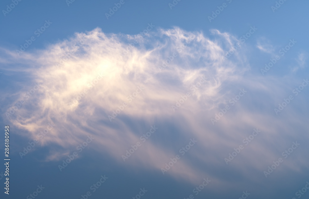 Fluffy white rose orange feather cloud in very quiet evening sky illuminated by the setting sun, just outside of Umea city, Vasterbotten, Northern Sweden. Isolated photo
