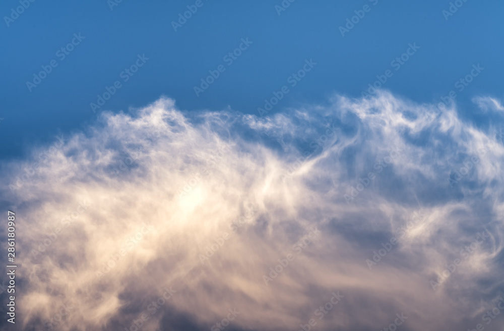 Fluffy white rose orange feather cloud in very quiet evening sky illuminated by the setting sun, just outside of Umea city, Vasterbotten, Northern Sweden. Isolated photo