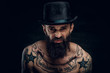 © Fxquadro - Portrait of strange funny man with hat, beard and a lot of tattooes at the dark background.