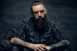 © Fxquadro - Bearded pensive man with tattooes is sitting on the armchair at dark room.