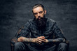 © Fxquadro - Bearded pensive man with tattooes is sitting on the armchair at dark room.
