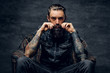 © Fxquadro - Bearded pensive man with tattooes is sitting on the armchair at dark room.
