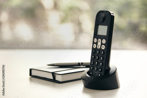 Fotografía Telefono inalambrico y libreta con fondo verde fuera de foco y luz natural