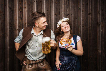 Poster - Junge Frau und mann mit Bierkrug und Brezel auf einem Holzhintergrund .Oktoberfest-Konzept 