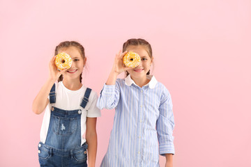 Poster - Portrait of happy twin girls with tasty donuts on color background