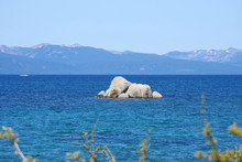 Panoramic View Of Blue Lake Tahoe With A Small Rock Island And Mountains With Patches Of Snow In The Distant Background On A Bright Summer Day