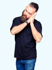 Young blond man wearing casual t-shirt sleeping tired dreaming and posing with hands together while smiling with closed eyes.