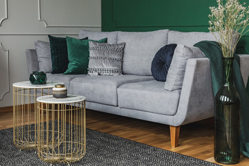 Two stylish small coffee tables with marble tops in front of elegant grey couch with emerald pillows