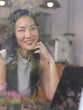 © Phuttharak - Asian woman sitting with her laptop in coffee shop smile through glass window.