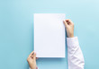 © asiandelight - close up hands holding  empty white blank letter paper size A4 for flyer or invitation mock up isolated on a blue background.
